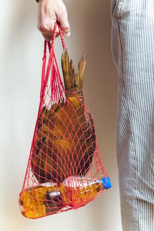 woven mesh bag with a large dried fish and a bottle of beer in his hand man in white trousers with a...