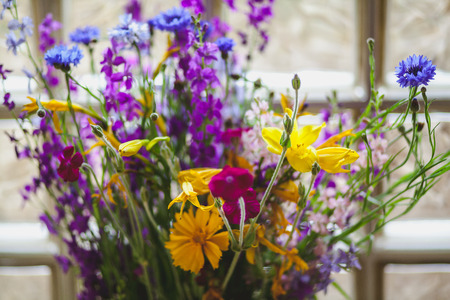 Flowers on the windowsill. A picturesque bouquet of wildflowers in a crystal vase stands against the window of transparent square glass blocksの写真素材