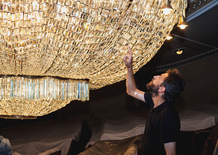 Revision of theatrical chandelier. A huge crystal theater chandelier hangs over the chairs. A man with a beard inspectsの写真素材