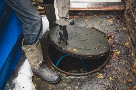 worker hand in the glove raises the metal cover of the sewer hatch on the street
