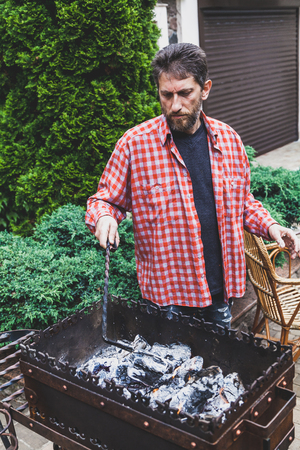 Preparation of coals in the grill. A man in a red checkered shirt picks hot coals in a forged brazier
の写真素材