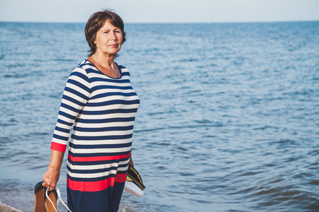 Woman walks along a sandy beach with sandals and sea cap in her handsの写真素材