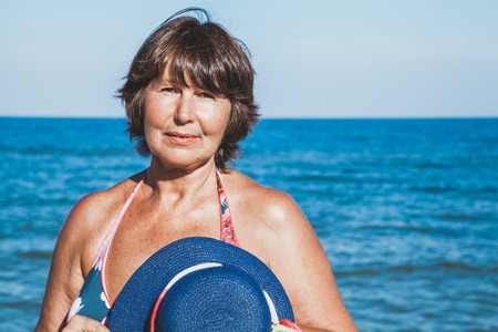 Elderly woman with beach hat in hand at sea sunny summer dayの写真素材