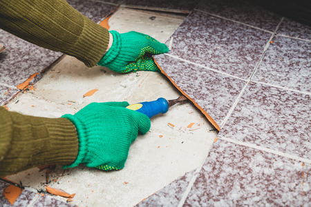 dismantling of tile. Hands in green working gloves undermine the broken tile with a chisel.の写真素材