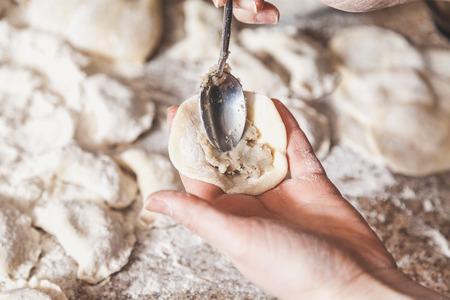 hand puts a stuffing in the dumpling with a teaspoon. Bottom of the table is a few raw dumplings in flourの写真素材