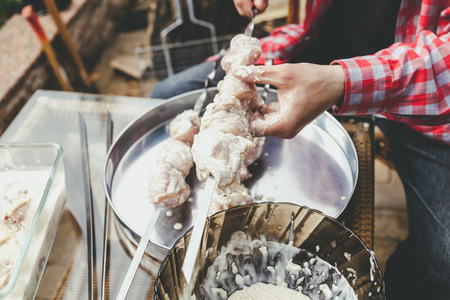 Preparation of shish kebab. Hands thread a piece of pickled meat on a steel skewer close-up. Next to the tray is a full skewerの写真素材
