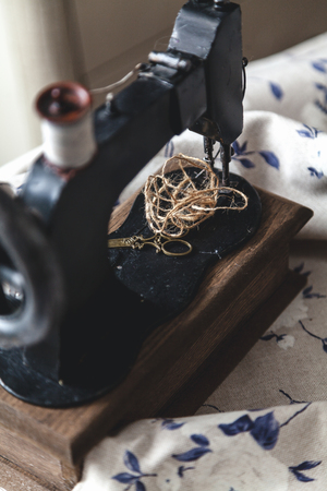 Vintage hand sewing machine and a skein of threads on a white cloth background with a blue closeup pattern.の写真素材
