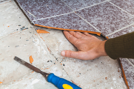 Repair of tiles. The hand is inserted into the gap between the tile and the floor. There is a chisel next to it.の写真素材