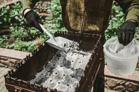 Cleaning the brazier after a picnic. Hands brush the brazier with a narrow spade. Ashes are piled in a plastic container
の写真素材