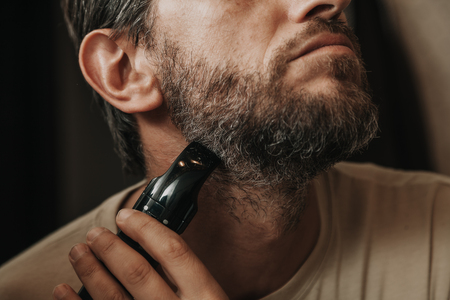beard trimmer trimmer. The man independently cuts his gray beard with a machine