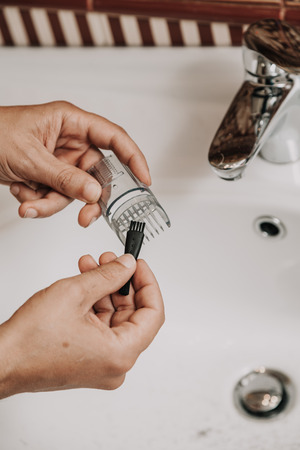 Cleaning the machine for cutting your beard. The man's hands clean the transparent trimmer attachment over the washbasin
の写真素材