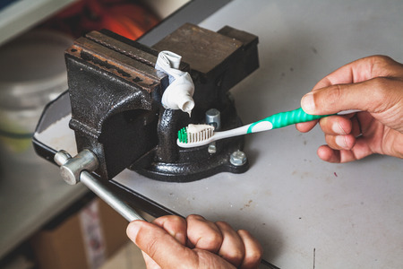 Very thrifty person squeezes the toothpaste from the tube onto a twisted brush clamped in the bench screwの写真素材