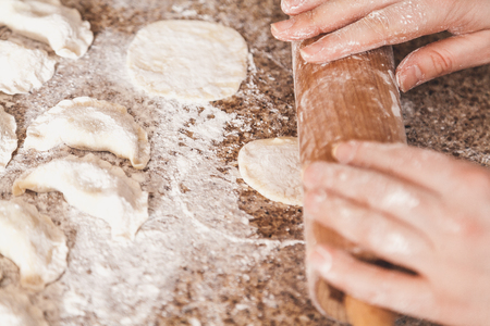 Preparation of vareniki. The woman's hands roll out the dough. Next to the table lie raw dumplings in white flour
の写真素材
