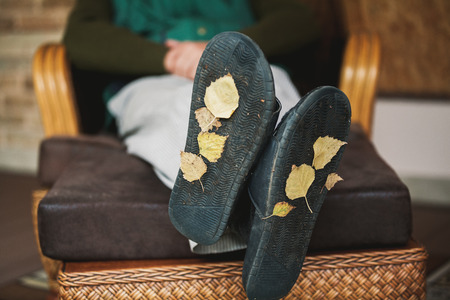 Traces of autumn. The tired man rests on the veranda in the chair. At the base of his house slippers, yellow autumn leaves stuck.の写真素材