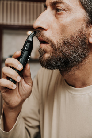 Haircut beard trimmer. A man cuts his mustache with a machineの写真素材