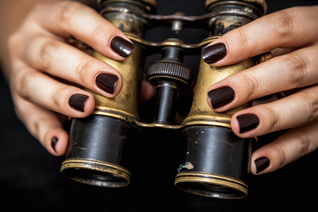 Binoculars and a woman. Beautiful female hands with manicure hold vintage metal binocularsの写真素材