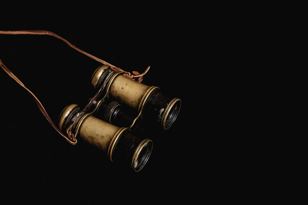 Vintage metal binoculars with a leather strap on a black backgroundの写真素材