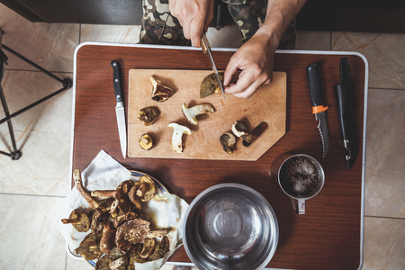 Processing of collected mushrooms. The man's hands cut fresh edible mushrooms on a wooden board. View from aboveの写真素材
