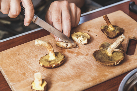 Processing of collected mushrooms. Hands of a man cut fresh edible porcini mushrooms on a wooden boardの写真素材