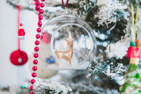 original Christmas tree toy is a brown deer inside a transparent ball weighing on a Christmas tree. Near the red garlandの写真素材