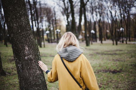 slender blonde in a bright yellow fashion coat walks in an autumn park. View from the backの写真素材