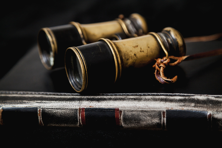 Vintage metal binoculars lie on a notepad in leather binding on a black backgroundの写真素材