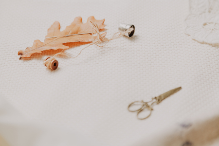 Autumn still life. A large yellow leaf of an oak and a coil with a thread lay on a white linen....