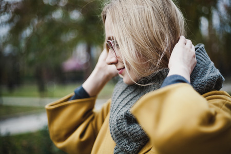 Portrait of a young woman in glasses with long blond hair in a yellow coat in an autumn parkの写真素材