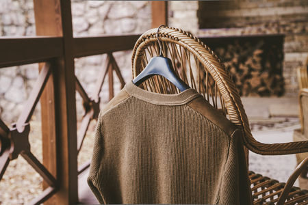 Autumn story. A woolen knitted jacket hangs on a hanger on the back of a wicker chair on the verandaの写真素材