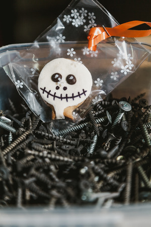Halloween in the workshop. Cookies for Halloween in a transparent package lies in a box with black screwsの写真素材