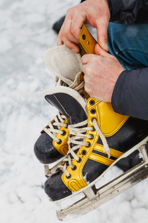 Skates in the hands. Hands hold leather black shoes with yellow inserts with steel skates.の写真素材