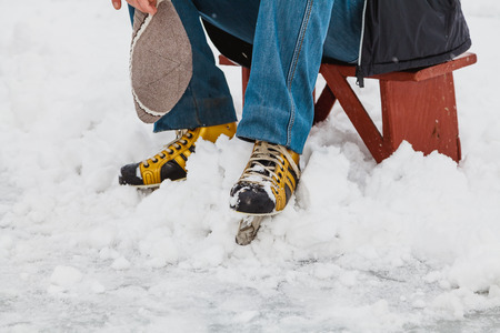 Rest after skiing. A man in skates sits on a wooden little bench in a natural open-air skating rink