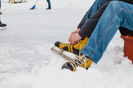 Hands tie a long string on the yellow leather boot of the modern skate. Around is loose snowの写真素材