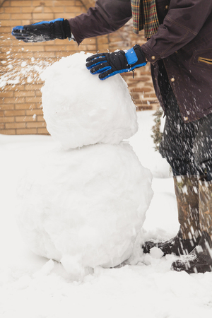 make a snowman. a man in ski gloves places a large snowball on a lower lump of a larger sizeの写真素材