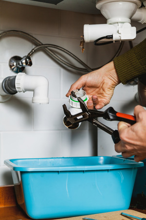 hands of the plumbing are dismantling the kitchen hydraulic shutter system with a pipe key close-up.の写真素材