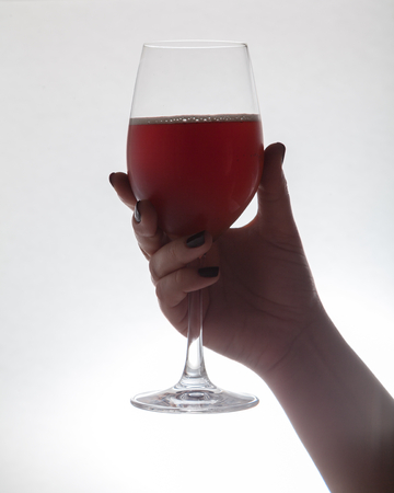 Woman hand is holding a glass wine goblet with wine on a white background close-upの写真素材