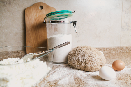 Cooking the pie. A piece of dough, flour, eggs and a glass jar are on a granite countertop.の写真素材