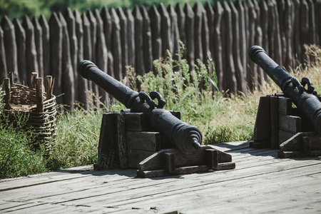 two ancient cast-iron cannons on a wooden carriage in an open-air museum. In the background a wooden palisadeのeditorial素材