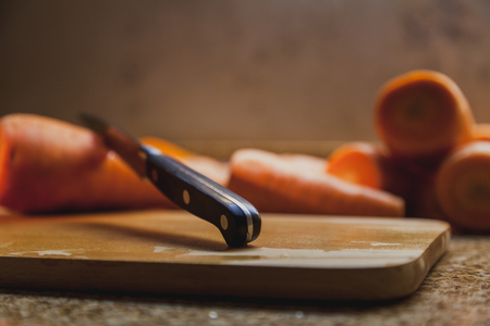 Cutting vegetables. Large ripe red carrot lies on a wooden board. There is a sharp knife sticking up in it.の写真素材