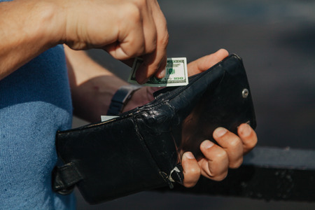 Toy money. A hand is hiding a miniature dollar bill in a black purseの写真素材