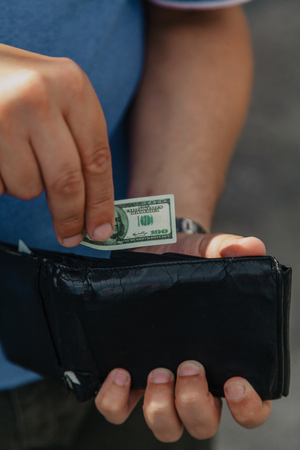 Toy money. A hand is hiding a miniature dollar bill in a black purse