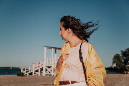 Portrait of a pretty curvy girl with long red hair and a bright yellow jacket on a sandy beachの写真素材