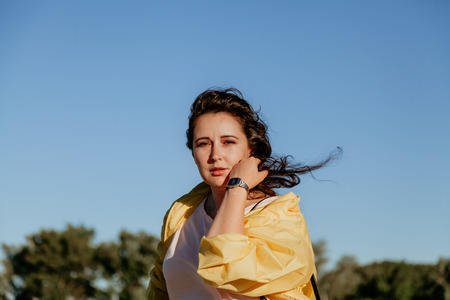 Portrait of a pretty curvy girl with long red hair and a bright yellow jacket against a blue skyの写真素材