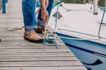 Male hands fastens the mooring rope of a white yacht on a wooden jetty bollard close-upの写真素材