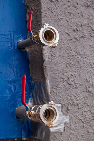 Two water fire hydrants of different diameters come out of the blue box against the gray wallの写真素材