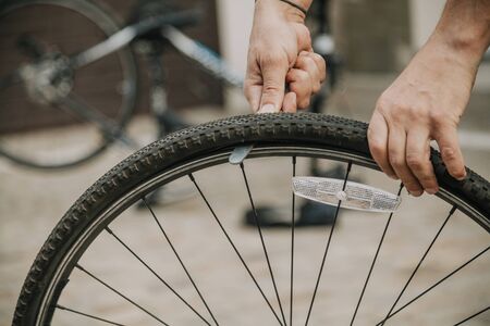 Hands remove the tire from the rim of the bicycle wheel with the help of a special flat tool close upの写真素材
