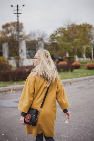 slender blonde in a bright yellow fashion coat walks in an autumn park. View from the backの写真素材