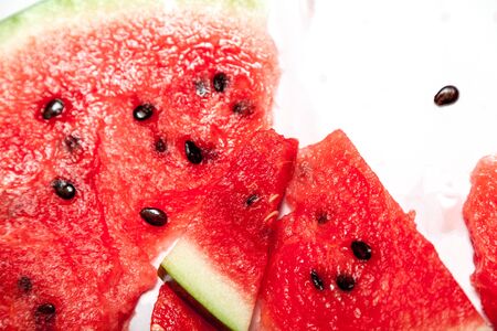Several slices of ripe red termelon are randomly laid out on a white background close-up. Some of...