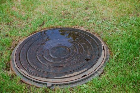 Sewer construction. Closed sewer well on green grass lawn
