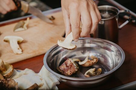 left hand puts chopped edible mushrooms in a metal bowlの写真素材